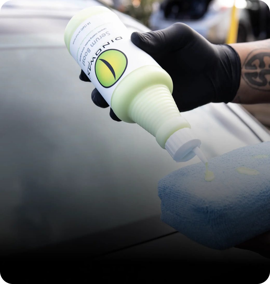 Gloved hand applying liquid from a bottle onto a blue sponge.