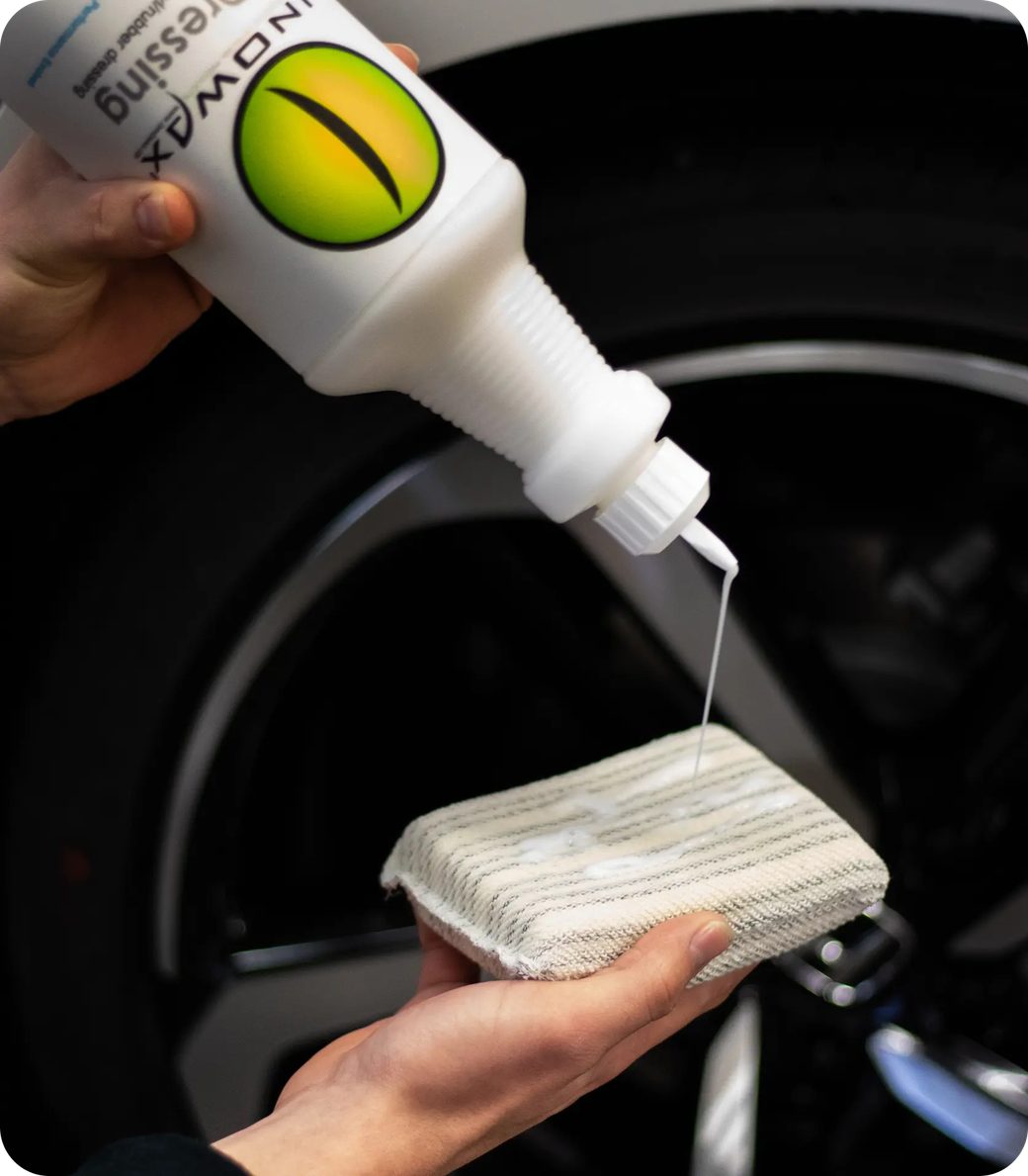 Person pouring liquid from a bottle onto a cloth near a car wheel.